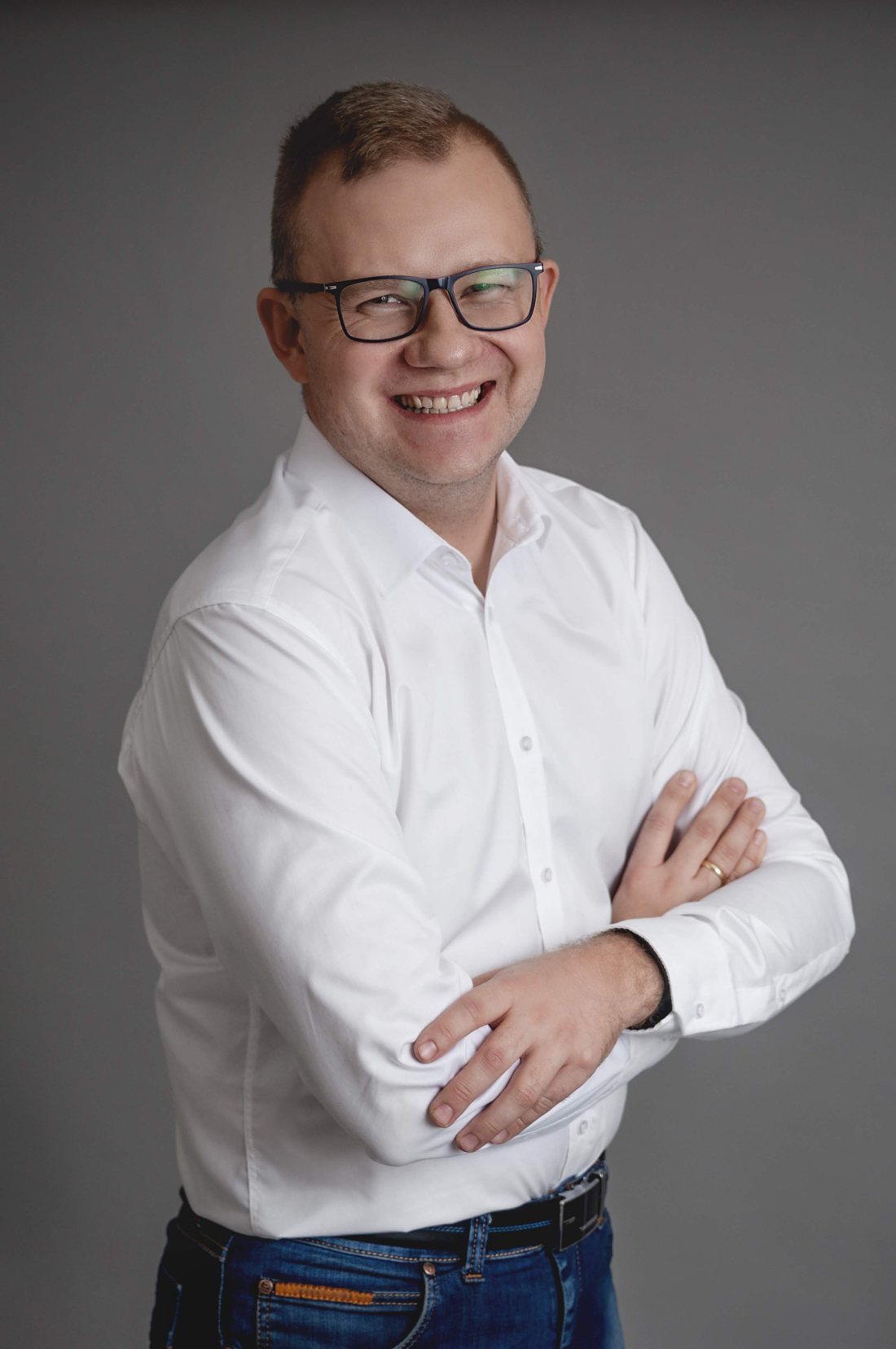 Łukasz Kosiński, uśmiechnięty, w białej koszuli, z założonymi rękami